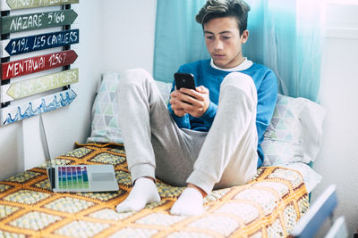 Full length of man using mobile phone while sitting on bed