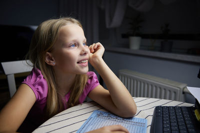 A smiling little european girl looks at the monitor screen and smiles.