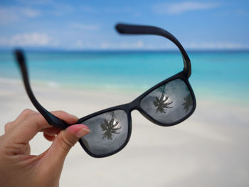Cropped hand of woman holding sunglasses at beach