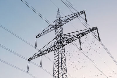 Low angle view of electricity pylon and flock of birds against clear sky