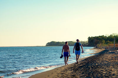 Rear view of people walking on beach against clear sky
