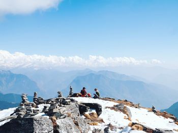 Friends sitting on snowcapped mountain peak against cloudy sky