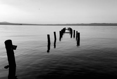 Silhouette people on wooden post in sea against sky