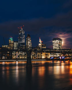 Illuminated buildings by river in city at night