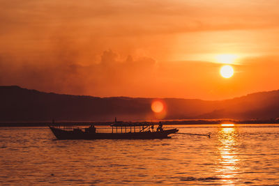 Silhouette boats in sea against orange sky