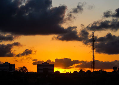 Silhouette built structures against dramatic sky during sunset