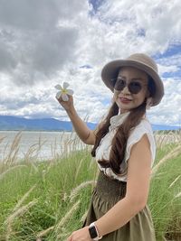 Young woman wearing sunglasses standing on field against sky