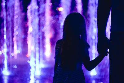 Midsection of man holding hands with daughter standing against illuminated fountain at night