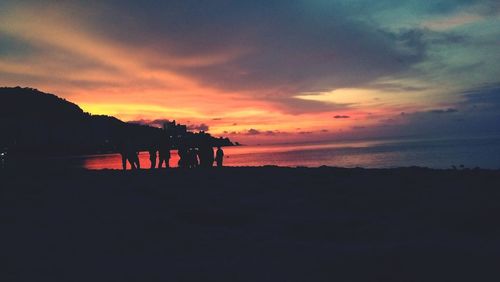 Silhouette people on beach against sky during sunset