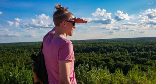 Young man shielding eyes while looking at forest