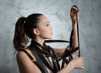 Young woman looking at film reel while standing against wall