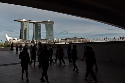 Silhouette people walking on footpath against marina bay sands