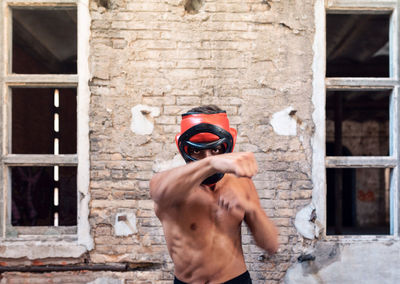 Portrait of young man punching while standing against wall