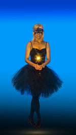 Portrait of female ballet dancer holding sparkler standing against blue background