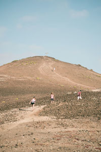 People walking on field by mountain against sky