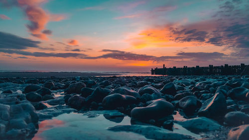 Rocks on beach against sky during sunset