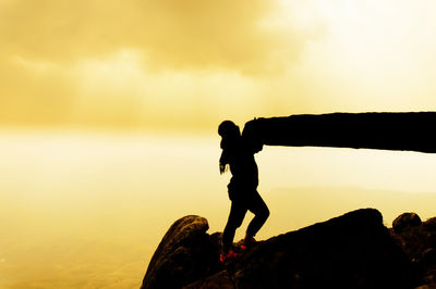 Silhouette woman holding rock formation against sky during sunset