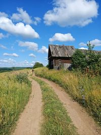 Footpath amidst field and houses against sky