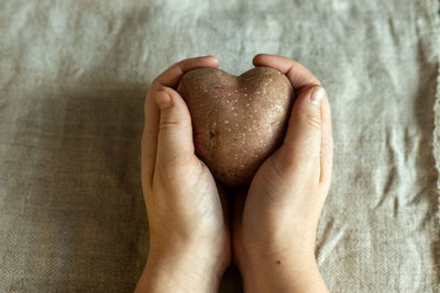 Female hands holding ugly vegetables potatoes in the shape of a heart on a background of linen cloth