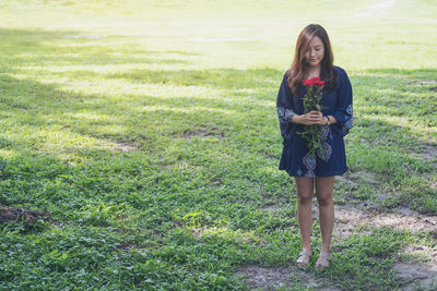 Smiling woman with bouquet standing on grassy field