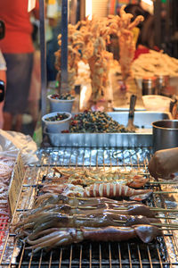 Cropped hand grilling squids on barbecue at street market