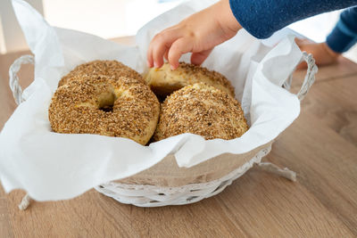 The child takes the bread from the bowl on the wooden kitchen table