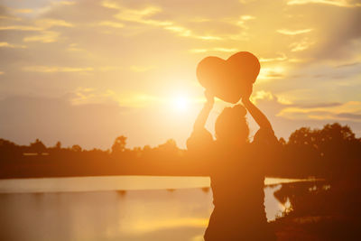 Silhouette woman standing by lake against sky during sunset