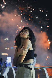 Young woman posing while standing against firework display
