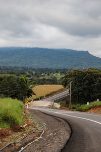 Empty road along trees and plants against sky