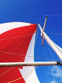 Low angle view of red and white canvas on boat mast against blue sky