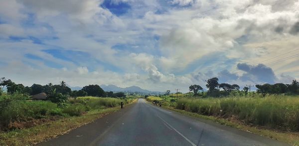 Empty road amidst field against sky