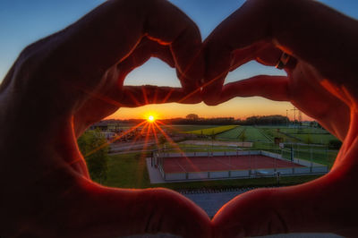 Midsection of man making heart shape against sky during sunset