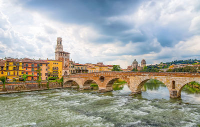 Arch bridge over river against cloudy sky