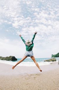 Rear view of woman with arms raised jumping against sea at beach