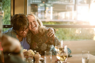 Smiling senior woman with arm around cheerful friend enjoying in restaurant