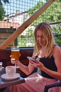 Woman using phone while having drink at cafe