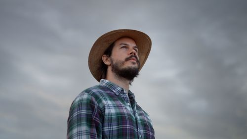 Bearded man wearing plaid shirt holding spikelet, reed, dry grass his mouth and looking at the sky