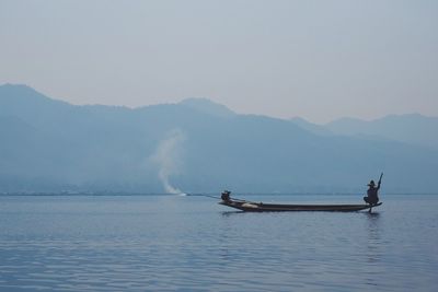 Fisherman sitting in boat on inle lake against sky during foggy weather