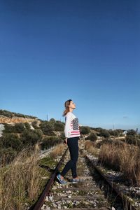 Full length side view of woman standing on railroad track against clear sky