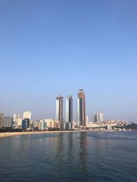 Sea by modern buildings against clear sky
