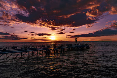 Silhouette pier over sea against sky during sunset