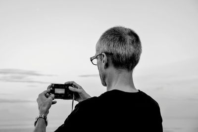 Portrait of man photographing with mobile phone against sky