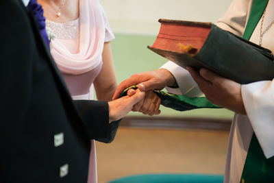 Midsection of bride and bridegroom taking wedding vows with priest at church