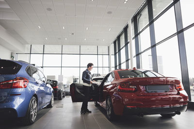 Senior woman looking inside car in showroom