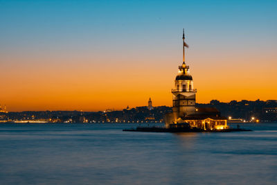 Illuminated buildings by sea against sky during sunset