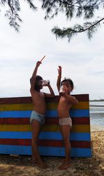 Full length of shirtless boy standing at beach against sky