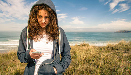 Young woman using mobile phone at beach against sky