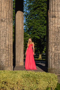 Full length portrait of young woman in pink evening gown standing at colonnade