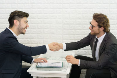 Businessmen shaking hands while sitting at table in office