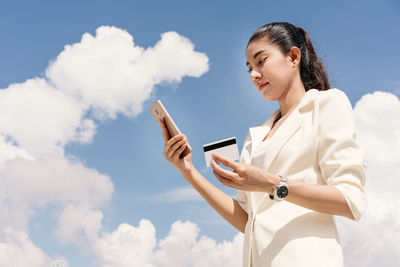 Low angle view of woman using smart phone against sky